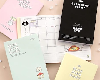 May include: Four 2027 Blah Blah Diary planners in pink, black, light blue, and yellow, featuring cartoon cat illustrations and Korean text. One planner is open to a monthly calendar page. Decorative stickers with Korean text are included.