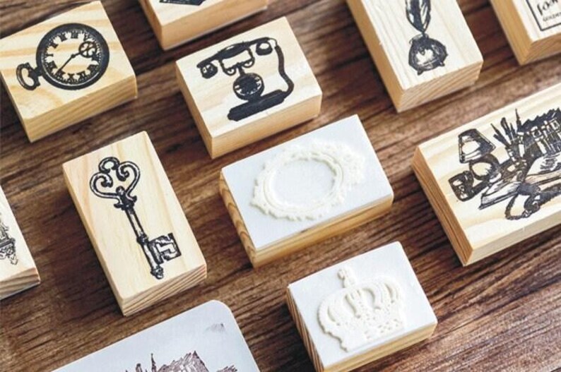 Op de afbeelding: Een verzameling houten stempels met verschillende ontwerpen, waaronder een klok, een telefoon, een sleutel, een kroon en een frame. De stempels zijn allemaal gemaakt van natuurlijk hout en hebben een vintage uitstraling.