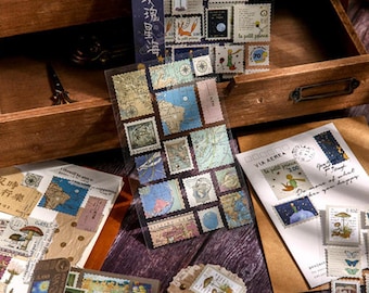 May include: A collection of decorative stickers and stamps featuring various designs, including maps, illustrations from "Le Petit Prince," and artwork. The stickers are arranged on a wooden surface, with some displayed in a wooden drawer.