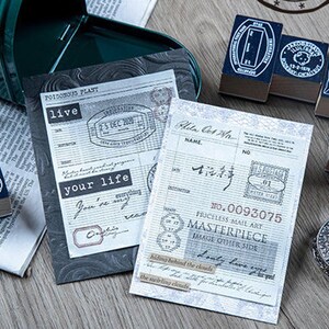 May include: A collection of vintage-style stamps, stationery, and ephemera. The scene includes several stamps with dark blue ink pads, printed paper, and a decorative metal object. The paper has text and stamps, with phrases like "live" and "your life".