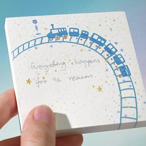 Könnte beinhalten: Ein weißer Notizblock mit einem blauen Zug, der einen Kreis mit goldenen Sternen umfährt. Der Notizblock trägt den Text "Everything happens for a reason."