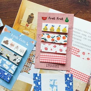Op de afbeelding: Twee sets decoratieve washi tape met kleurrijke patronen. De ene set heeft een fruitthema met peren, sinaasappels, aardbeien en een ruitpatroon. De andere set heeft een schattig dieren thema met zwanen, een panda, een vos en een hond. Beide sets hebben de tekst "TWILIGHT" onderaan.