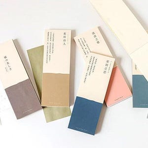 Puede incluir: Seis marcadores de diferentes colores con texto japonés. Los marcadores son todos rectangulares y tienen una mitad superior blanca y una mitad inferior de color. El texto en los marcadores está en negro.