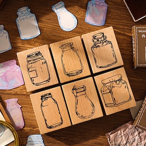 May include: A set of eight wooden stamps featuring different designs of glass jars. The stamps are arranged in two rows of four. The stamps are made of natural wood and have a light brown colour. The jars are drawn in black ink and have a vintage style. The stamps are perfect for adding a touch of whimsy to your crafting projects.