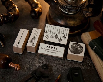 May include: A collection of wooden stamps with various designs, including light fixtures, a full moon, and phases of the moon. The stamps are arranged on a dark surface with other vintage-style objects.