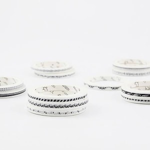 以下が含まれることがあります： 黒の模様がついた白い和紙テープのロールが6つセットになっています。テープはロール状になっており、クラフト、デコレーション、ジャーナリングに使用できます。