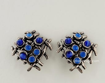 May include: A pair of silver tone earrings with a geometric design featuring blue and dark blue stones.