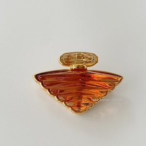 Op de afbeelding: Een vintage parfumflesvormige broche met een goudkleurig montuur en amberkleurig glas. De broche heeft een waaiervormig ontwerp met een rechthoekige bovenkant. De tekst "aka bijoux_vintage" is zichtbaar.