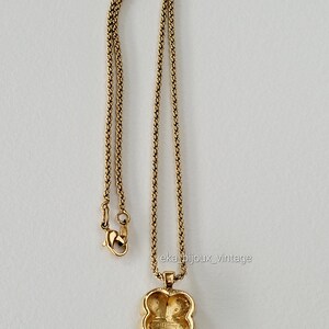 K&ouml;nnte beinhalten: Goldkette mit einem vierbl&auml;ttrigen Kleeblatt-Anh&auml;nger. Der Anh&auml;nger hat ein erhabenes Design und die Worte "Guess" sind auf der R&uuml;ckseite sichtbar.