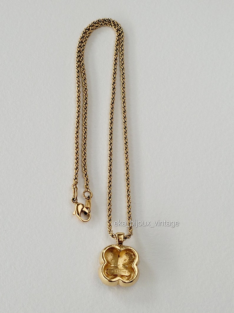K&ouml;nnte beinhalten: Goldkette mit einem vierbl&auml;ttrigen Kleeblatt-Anh&auml;nger. Der Anh&auml;nger hat ein erhabenes Design und die Worte "Guess" sind auf der R&uuml;ckseite sichtbar.