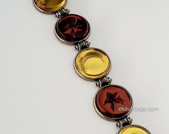 Könnte beinhalten: Ein Vintage-Armband mit fünf runden, facettierten Glasperlen. Die Perlen wechseln sich in den Farben Gelb und Bernstein ab. Die Bernsteinperlen haben ein eingraviertes Sternmuster. Das Armband hat einen silbernen Verschluss.