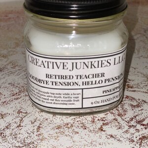 Pode incluir: Uma vela branca num frasco de vidro transparente com uma tampa preta. O rótulo diz "Creative Junkies LLC" e "Professor aposentado, Adeus tensão, Olá pensão". A vela é etiquetada como "Abacaxi" e pesa 9 oz.