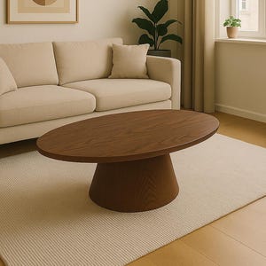 以下が含まれることがあります： 明るいベージュのソファ、濃い茶色の楕円形のコーヒーテーブル、ベージュのラグが特徴のリビングルーム。壁には額入りの抽象芸術作品が飾られています。部屋はニュートラルな色使いで、自然光が入ります。