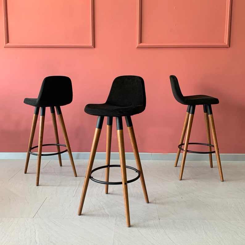 May include: Three black bar stools with wooden legs and black metal accents. The stools have a padded seat and a backrest.