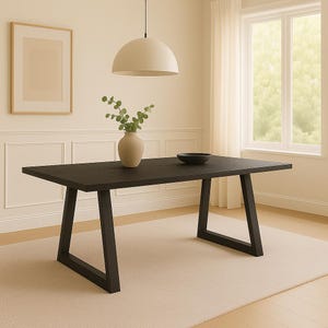 Puede incluir: Una mesa de comedor rectangular marrón oscuro con patas anguladas. Un cuenco negro y un jarrón beige con hojas verdes están sobre la mesa. Una alfombra beige está debajo de la mesa.
