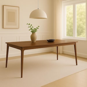 Puede incluir: Una mesa de comedor rectangular de madera con patas anguladas. Un jarrón con vegetación y un cuenco negro están sobre la mesa. La habitación tiene una paleta de colores neutros con una alfombra beige y una ventana con luz natural.
