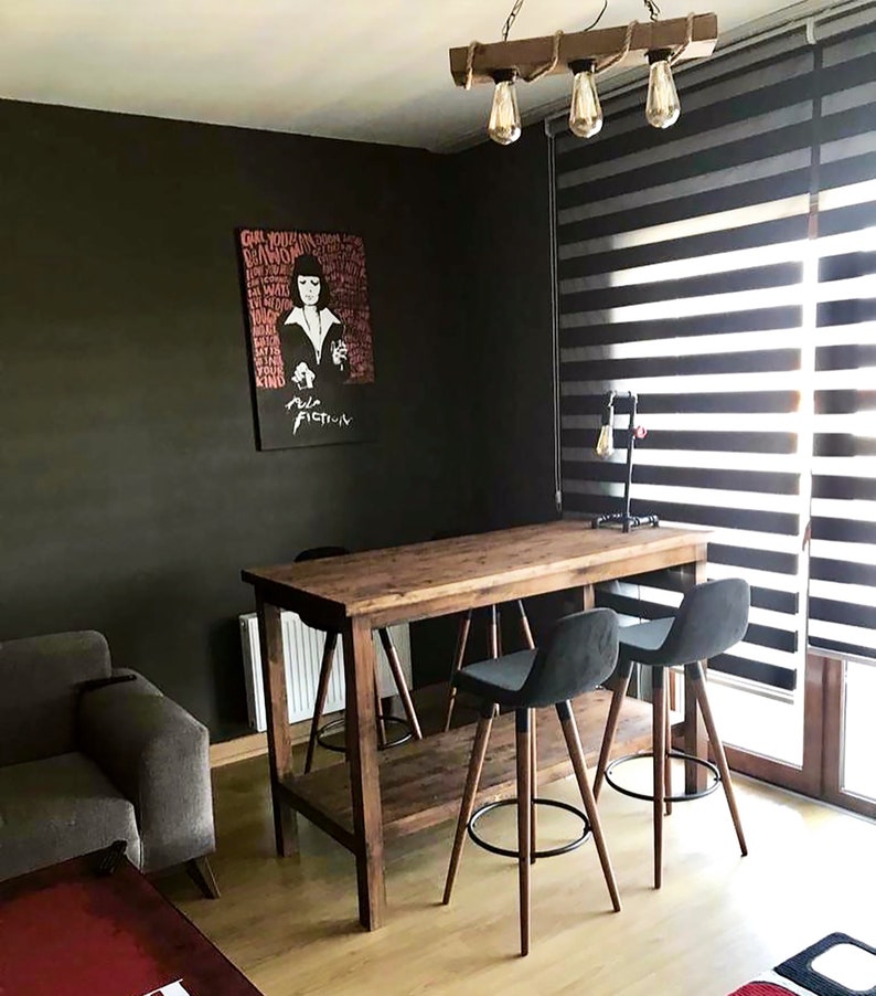 May include: A rustic wooden table with a metal frame. The table has a shelf underneath and is paired with three black bar stools. The table is in a room with a dark grey wall and a window with black blinds.
