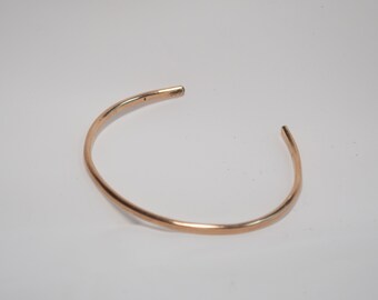 May include: A simple gold bangle bracelet. The bracelet is made of a single, thin piece of metal that is bent into a circle.