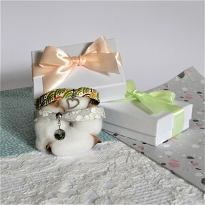 May include: A set of three bracelets with a heart charm, wrapped in white gift boxes with pink and green ribbon. The bracelets are made of fabric with a floral pattern.