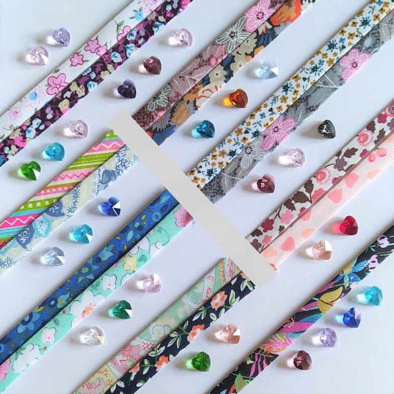 May include: Assortment of colorful fabric strips with various patterns, including floral, geometric, and abstract designs. The strips are arranged in a diagonal pattern and adorned with small, iridescent glass beads.