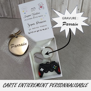 Può includere: Un portachiavi a forma di cuore dorato e un portachiavi rotondo argentato, entrambi incisi con la parola "Parrain". È incluso anche un portachiavi con controller nero e rosso. L'immagine mostra anche una carta personalizzata con testo.