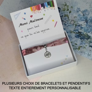 Peut inclure: Une boîte cadeau blanche contenant un bracelet à motif rose et blanc. La boîte contient une carte à l'intérieur qui dit "Merci Maîtresse pour tout ce que tu m'as appris..." Le bracelet est orné d'un charme en argent en forme d'arbre.