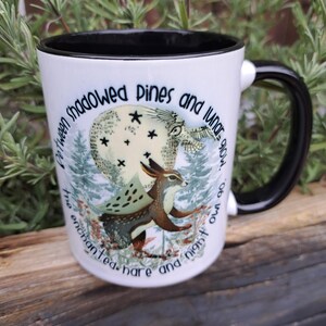 The enchanted hare and night owl mug in use, filled with a warm beverage. Styled in a cozy setting with natural elements, emphasizing its appeal to those who appreciate nature, the moon, and mystical themes. An ideal gift for fans of fantasy and woodland creatures.