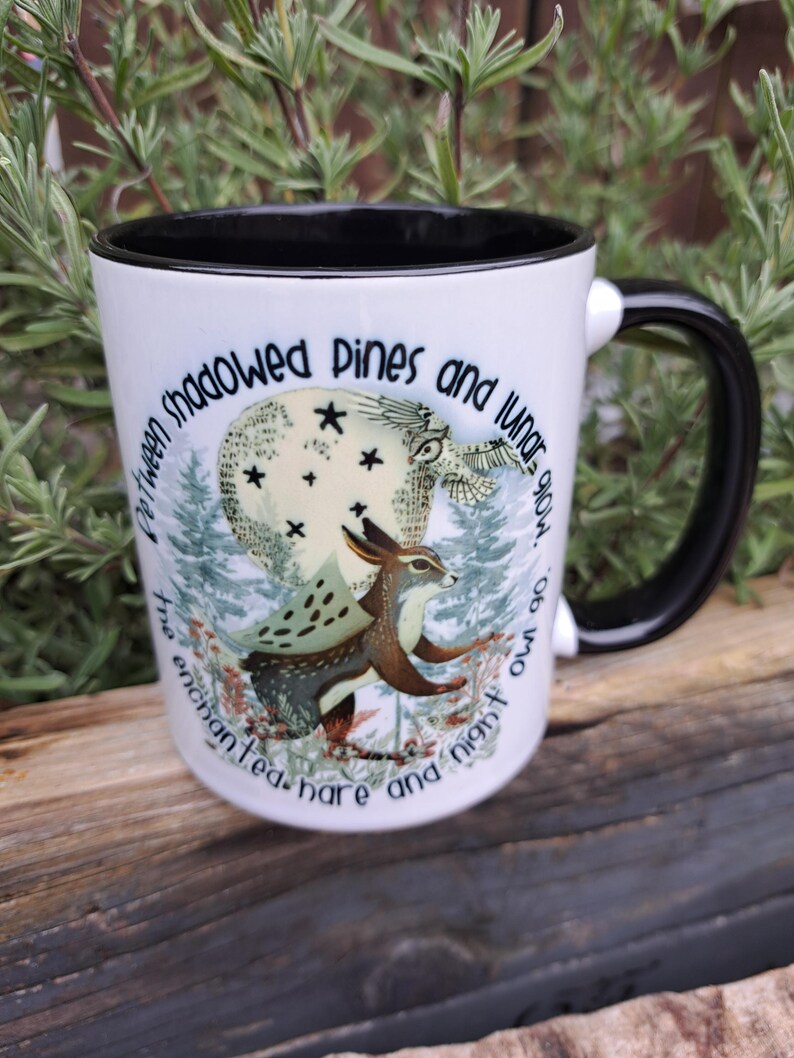 The enchanted hare and night owl mug in use, filled with a warm beverage. Styled in a cozy setting with natural elements, emphasizing its appeal to those who appreciate nature, the moon, and mystical themes. An ideal gift for fans of fantasy and woodland creatures.