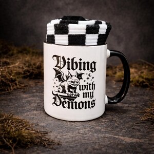 Gothic mug and socks gift set featuring a bold “Vibing with my demons” design and black and white checkered socks presented inside the mug.