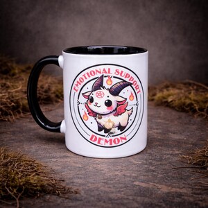 Cute alternative two-tone 11oz mug featuring a kawaii gothic demon character with “Emotional Support Demon” text. Designed with a mix of dark humour and playful style, photographed on a moody stone background