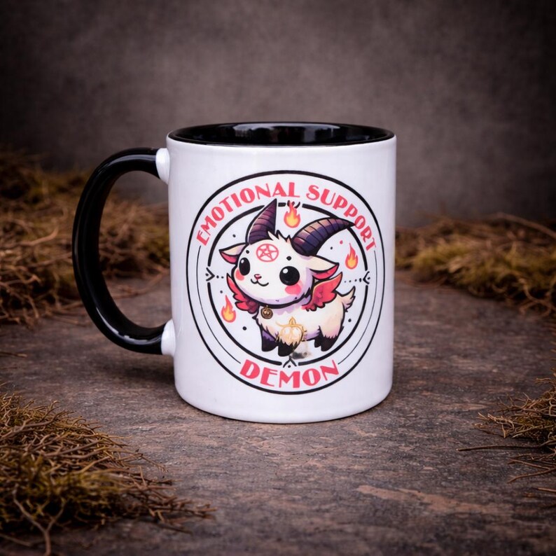 Cute alternative two-tone 11oz mug featuring a kawaii gothic demon character with “Emotional Support Demon” text. Designed with a mix of dark humour and playful style, photographed on a moody stone background