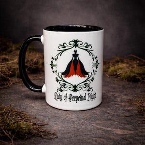Black and white ceramic two-tone mug featuring “Lady of Perpetual Night” design with gothic styling and elegant dark artwork. Photographed on a textured stone background.