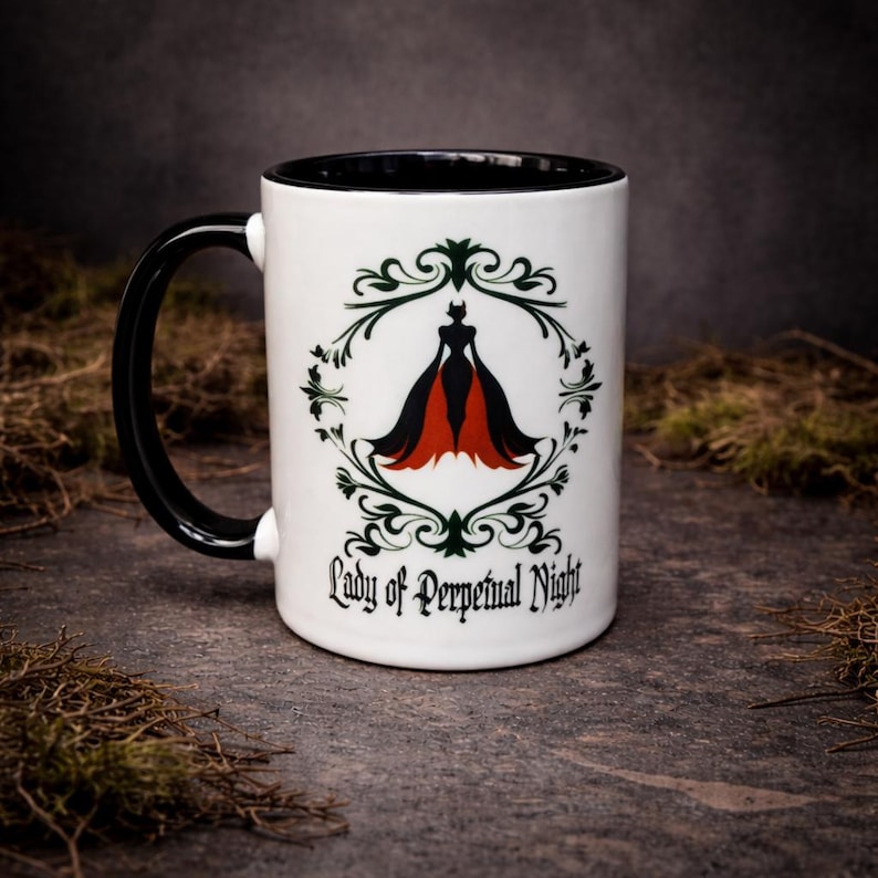 Black and white ceramic two-tone mug featuring “Lady of Perpetual Night” design with gothic styling and elegant dark artwork. Photographed on a textured stone background.