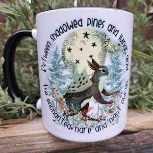 A high-quality 11oz ceramic mug featuring an original illustration of an enchanted hare and night owl under a glowing moon, surrounded by shadowed pine trees. The design includes the quote: "Between the shadowed pines and lunar glow, the enchanted hare and night owl go." Perfect for nature lovers and those with a mystical aesthetic.
