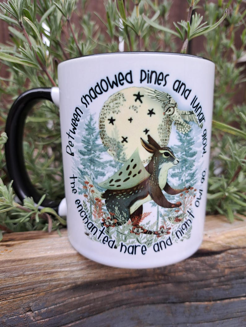 A high-quality 11oz ceramic mug featuring an original illustration of an enchanted hare and night owl under a glowing moon, surrounded by shadowed pine trees. The design includes the quote: "Between the shadowed pines and lunar glow, the enchanted hare and night owl go." Perfect for nature lovers and those with a mystical aesthetic.