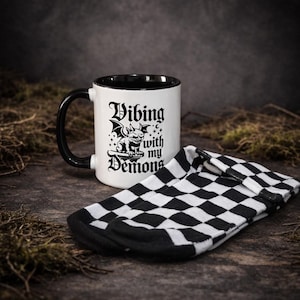 Alternative gift set including a gothic mug with “Vibing with my demons” slogan and black and white checkered socks. Shot in a dark, textured setting for a moody feel