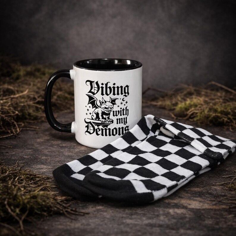 Alternative gift set including a gothic mug with “Vibing with my demons” slogan and black and white checkered socks. Shot in a dark, textured setting for a moody feel