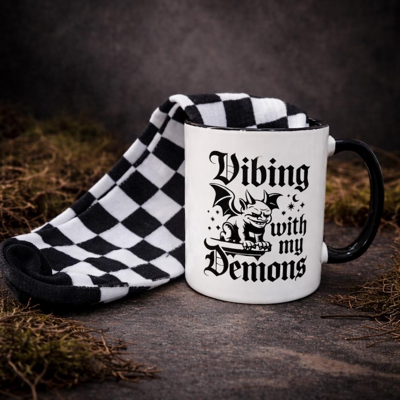 Gothic gift set featuring a black and white 11oz ceramic mug with “Vibing with my demons” design and black and white checkered socks. Styled on a textured stone background with a moody, alternative aesthetic