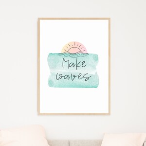 May include: A framed print with a watercolor background in shades of blue and pink. The print features a sun with rays and the text "Make Waves" in black.