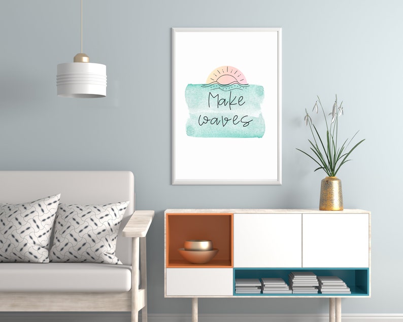 May include: A framed print with a watercolor background in shades of blue and green. The print features a simple line drawing of a sun setting over the ocean with the text "Make Waves" in black.