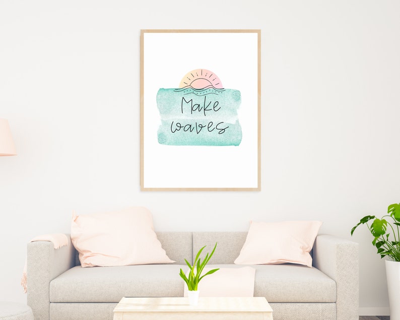 May include: A framed print with a watercolor background in shades of blue and pink. The print features a sun with rays and the text "Make Waves" in black.