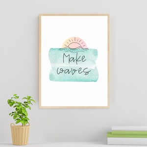 May include: A framed print with a watercolor background in shades of blue and green. The print features a simple line drawing of a sun setting over a wavy line, with the text "Make waves" written below.