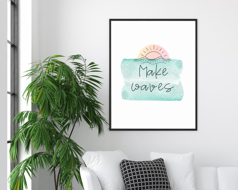 May include: A framed print with a watercolor background in shades of blue and green. The print features a stylized sun with a pink and orange gradient and the text "Make waves" in black.