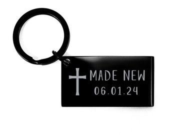 May include: Black metal keychain with a cross and the text "MADE NEW 06.01.24"