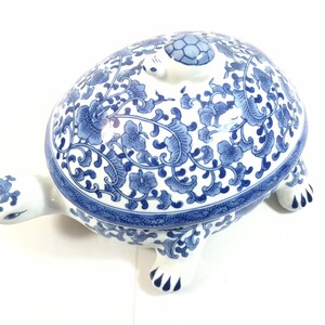 May include: A ceramic turtle-shaped lidded box featuring a white base with intricate blue floral and vine patterns. The lid includes a small sculpted turtle figure on top, and the turtle's head and feet are decorated with matching blue floral motifs.