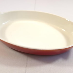 Op de afbeelding: Ovale ovenschaal met een rode buitenkant en een crèmekleurige binnenkant. De schaal heeft twee handvatten en is ontworpen voor gebruik in de oven. Een eenvoudig, functioneel stuk voor koken en serveren.
