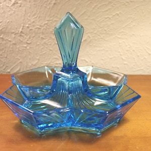 May include: A light blue glass serving dish with a central handle and three individual compartments. The dish has a geometric design and is perfect for serving snacks or appetizers.