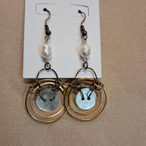 May include: A pair of gold hoop earrings with a white pearl and a mother-of-pearl button on each earring.