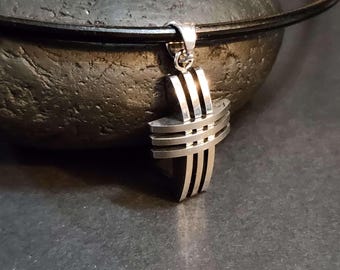 May include: A silver pendant in the shape of a cross with multiple horizontal lines. The pendant is hanging from a black leather cord.