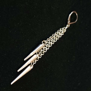 May include: A silver earring with a long chain and three silver spikes hanging from it.